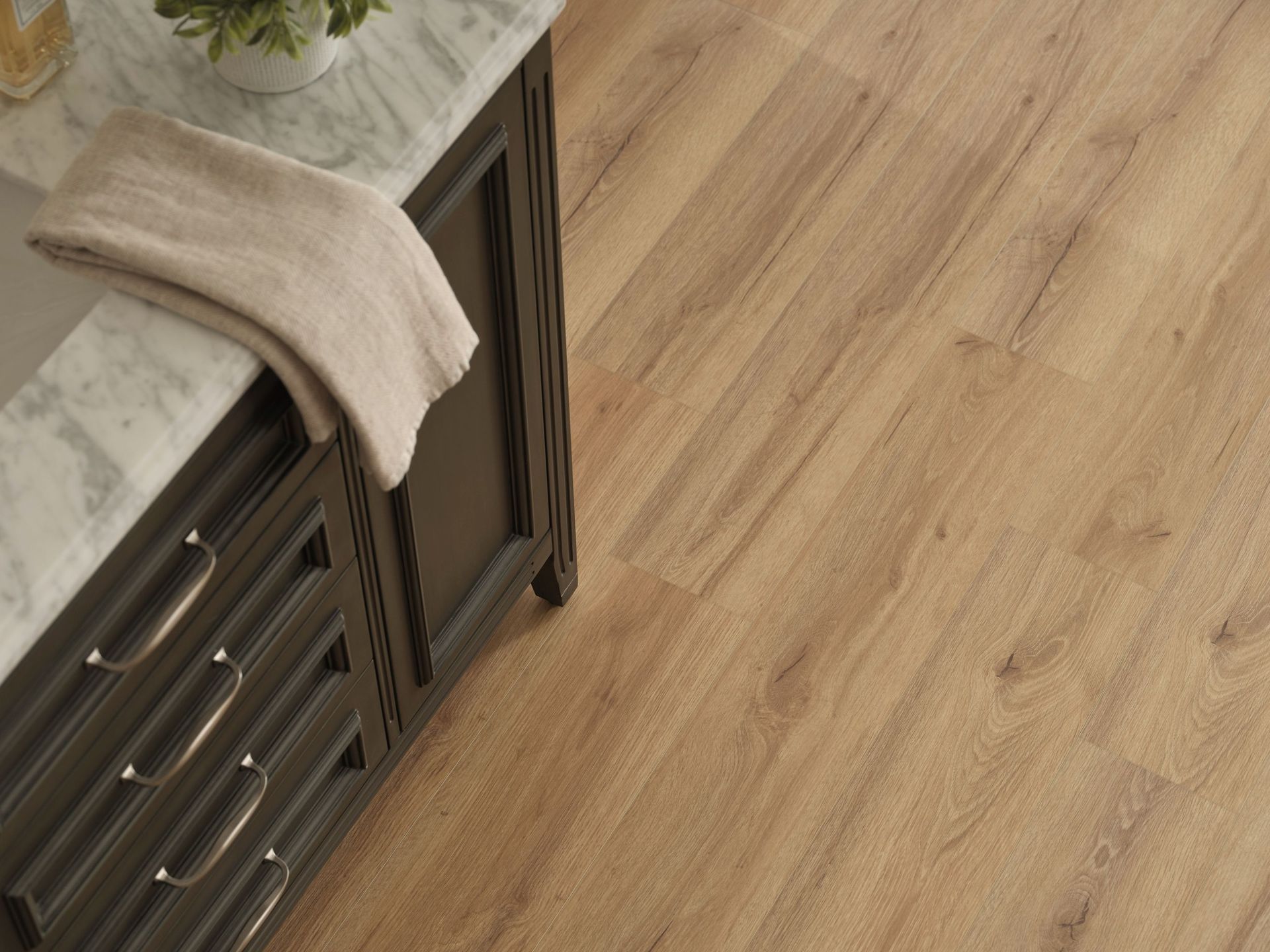 Bathroom with brown wood-look flooring next to a dark vanity with a marble countertop. A towel rests on the countertop.