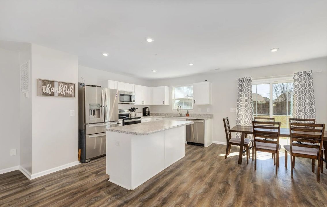 Open-concept kitchen with white cabinets, stainless steel appliances, a center island, and a dining table.