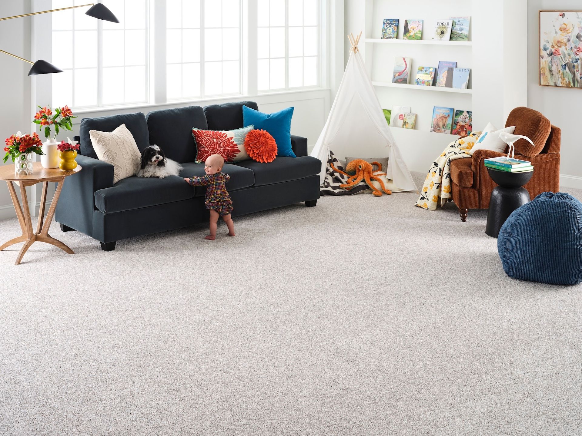 Child playing in a light-carpeted playroom with a couch, reading nook, and tent.