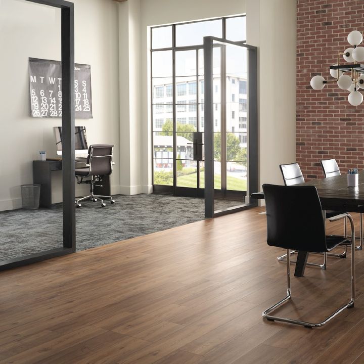 Office with glass walls, brick wall, dark wood floors, modern furniture, and a view of a building.