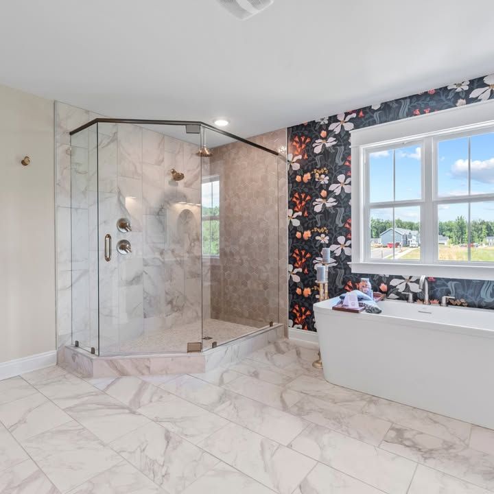 Modern bathroom with glass shower, freestanding tub, marble tile, and floral wallpaper.