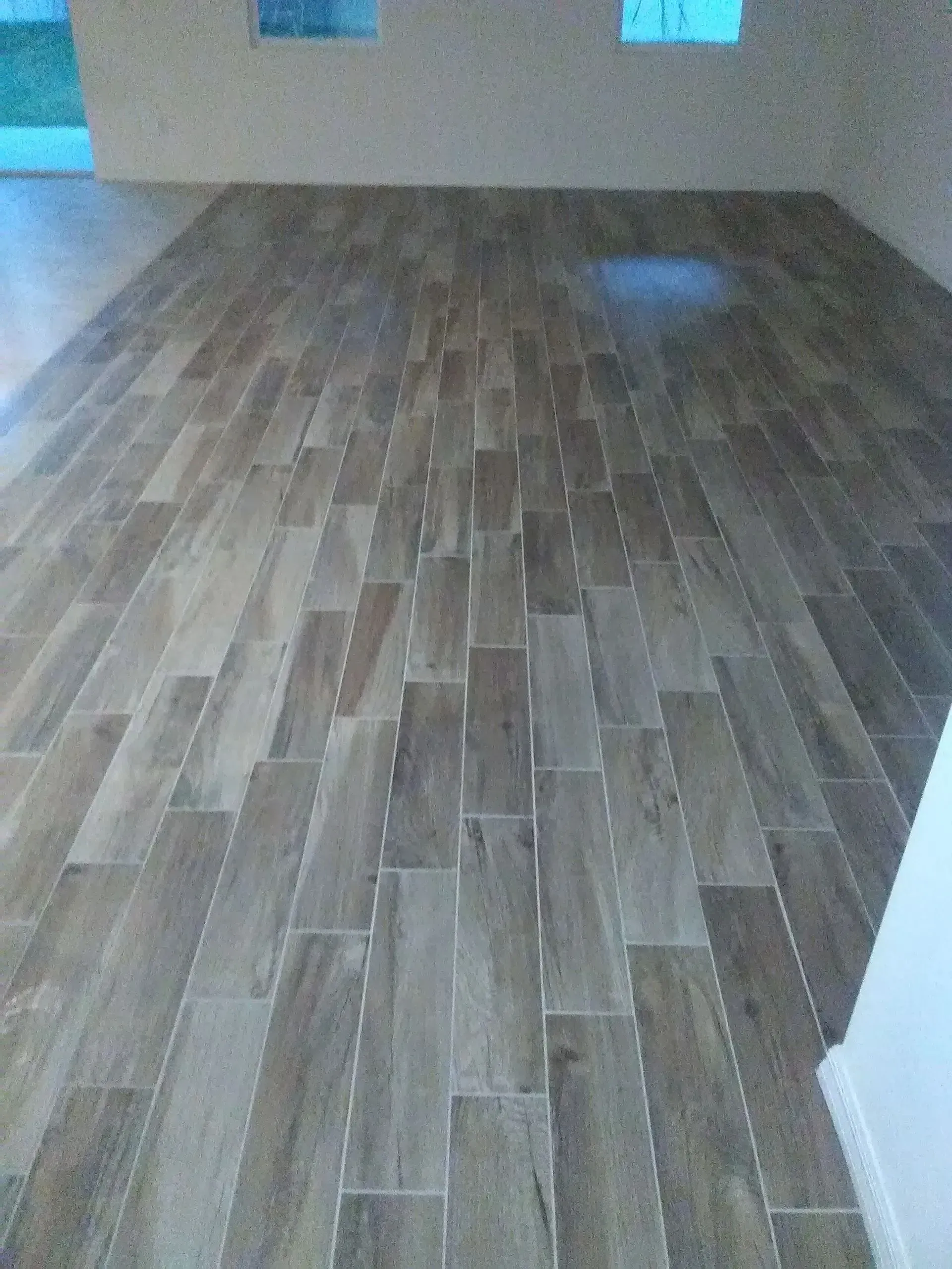 Wooden tile floor in a room with two small windows and white walls.