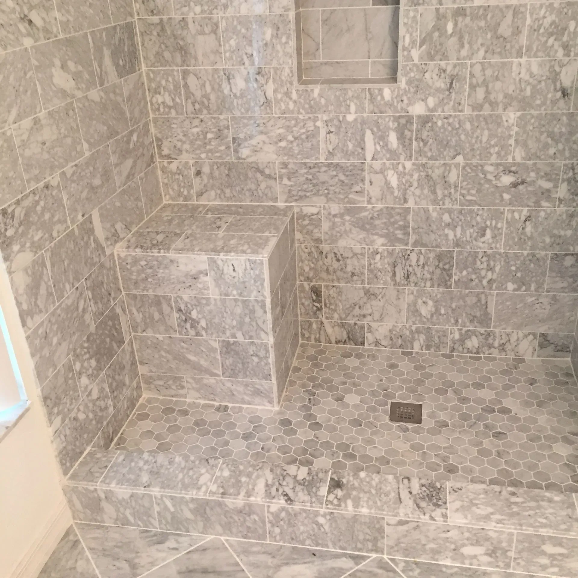 Gray marble tiled shower with built-in bench and hexagonal floor tiles.