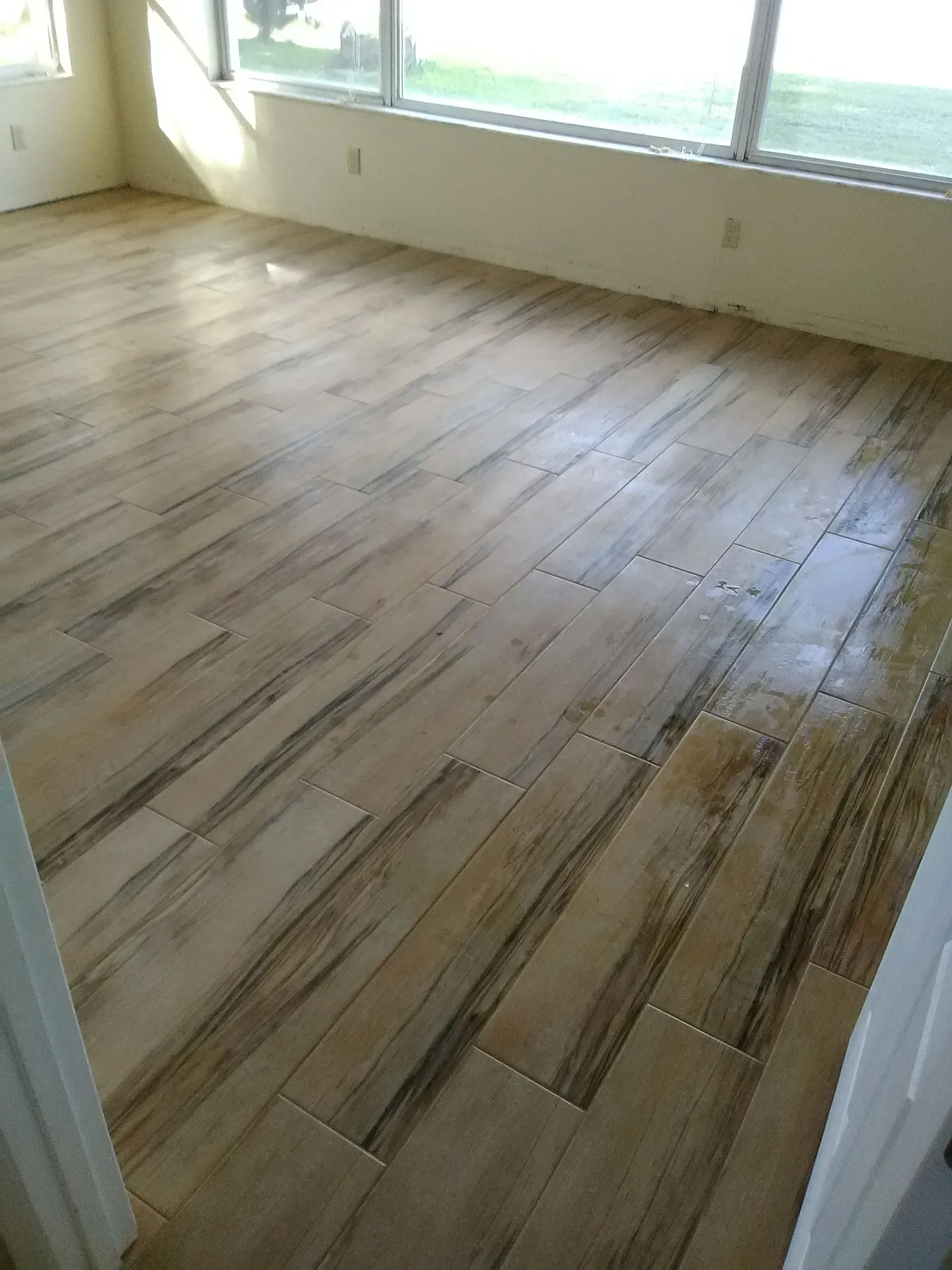 Wood-look tile flooring in a sunlit room with large windows.