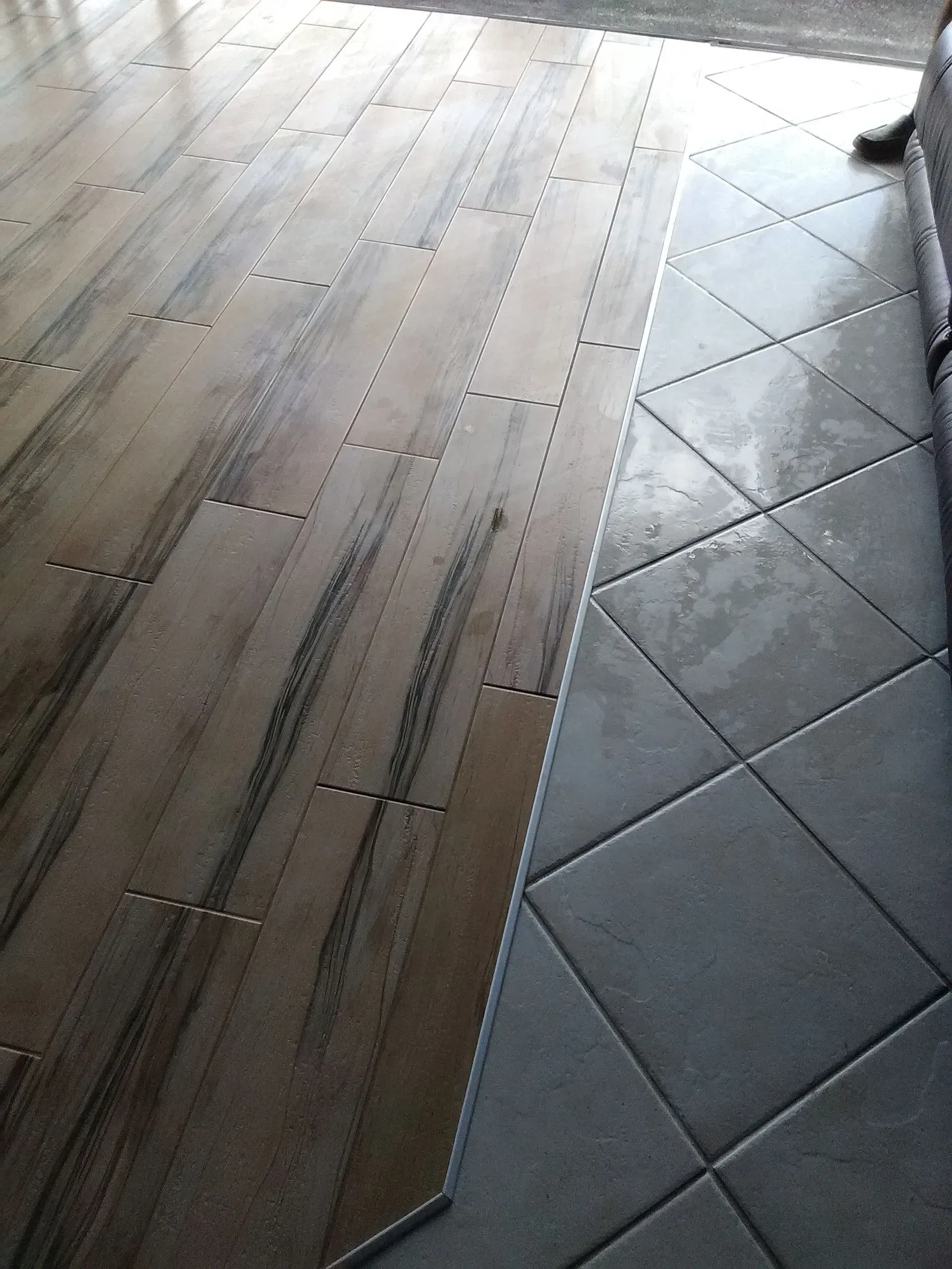 Wooden floor planks and gray diamond-pattern tiles meet on a floor.