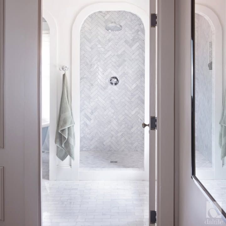 Bathroom interior with arched shower entry, herringbone tile, and towel.