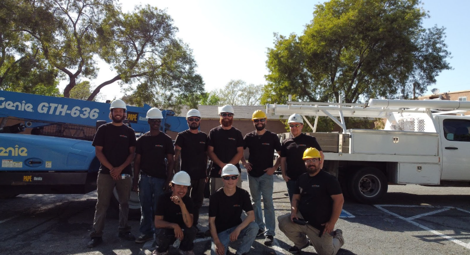 A group of construction workers pose for a picture in front of a genie truck
