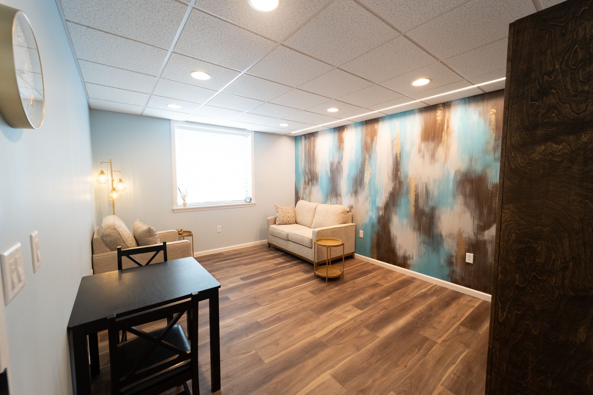 A finished basement with seating area, a black table, and a decorative blue and brown mural.