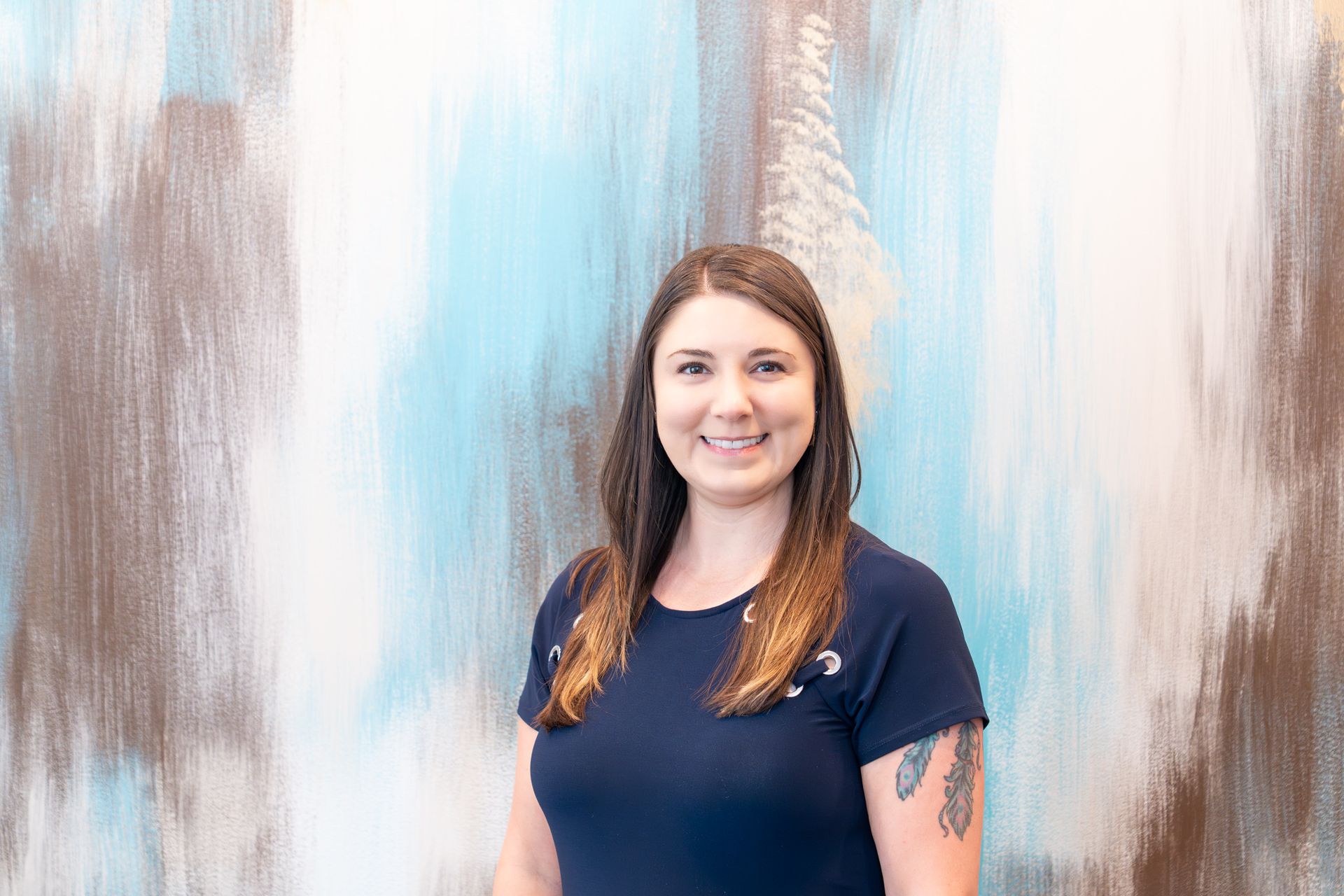 Woman in a dark blue shirt smiles in front of a blue and brown abstract painting.