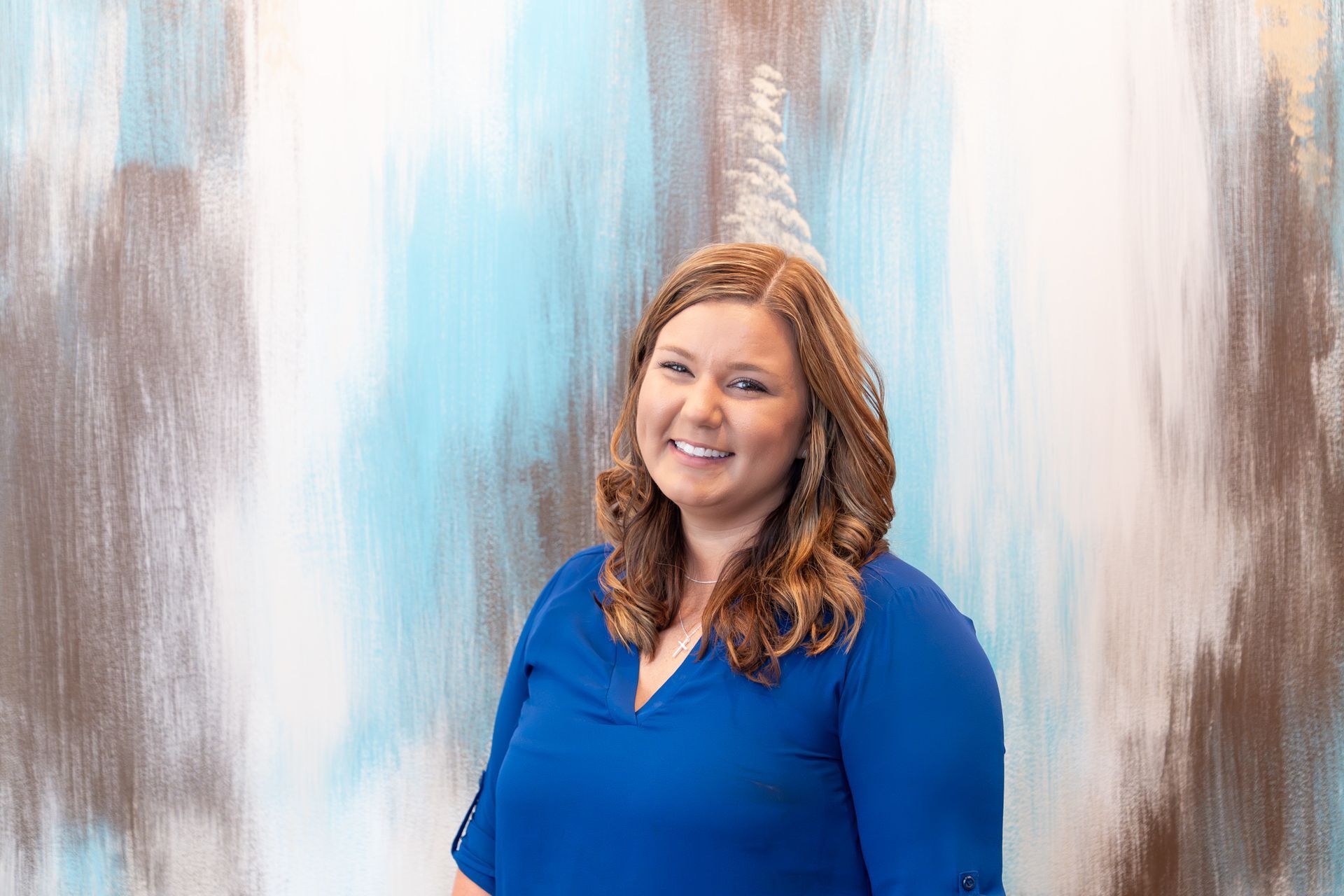 Woman smiling, wearing a blue shirt, in front of a blue and brown painted wall.
