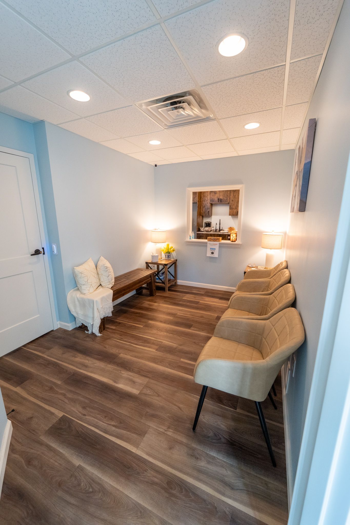 Waiting room with light blue walls, wood floor, chairs, and bench.