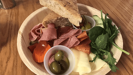 A plate of food with meat, cheese, olives, and bread on a wooden table.