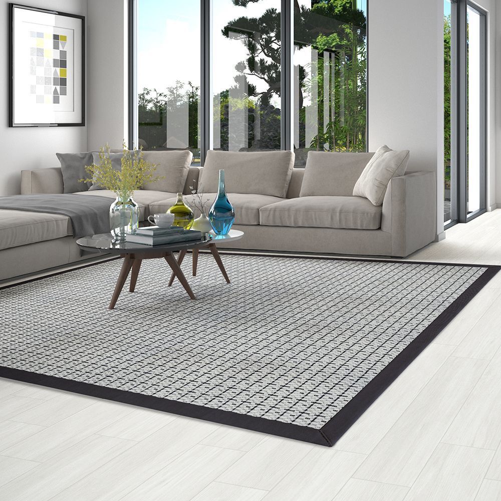 Living room with gray sofa, patterned rug, glass coffee table, and large windows.