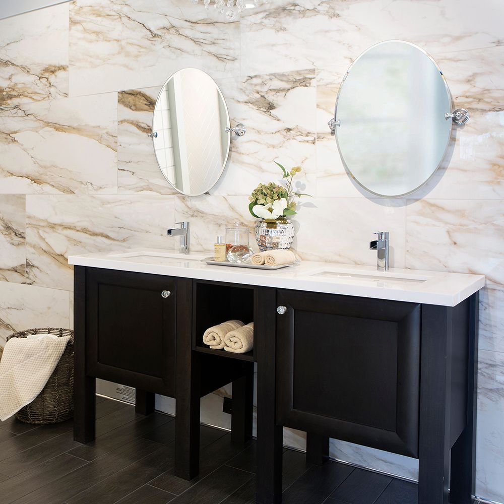 Bathroom with a black double vanity, white countertop, oval mirrors, and marble wall tiles.