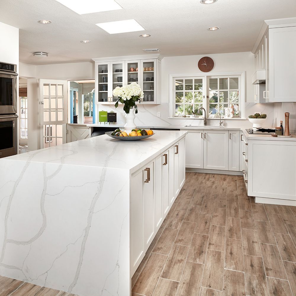 White kitchen with large island, quartz countertops, wooden floors, and white cabinetry.