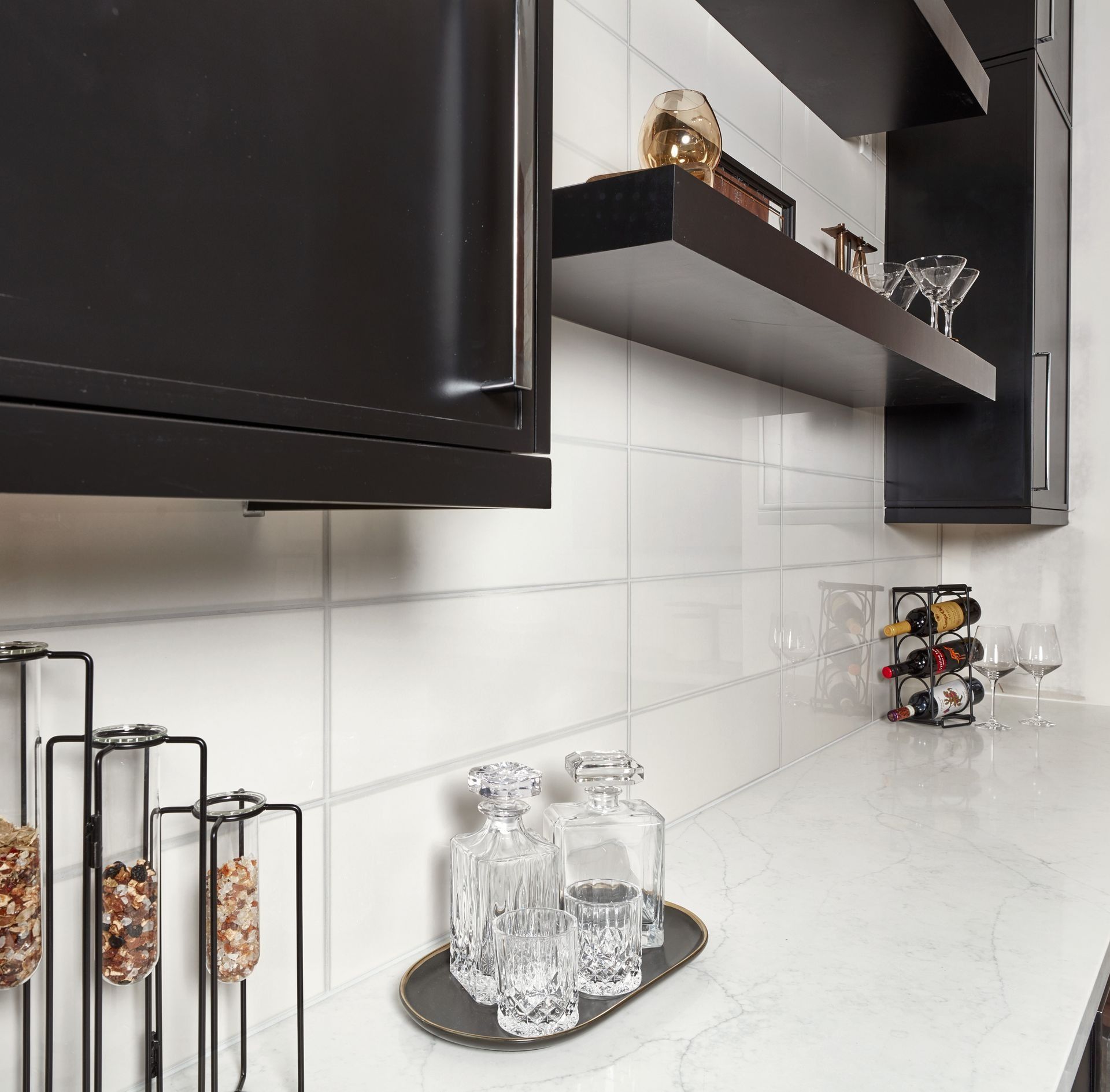 Modern kitchen with black cabinets, white countertops, shelves with liquor bottles and decor.