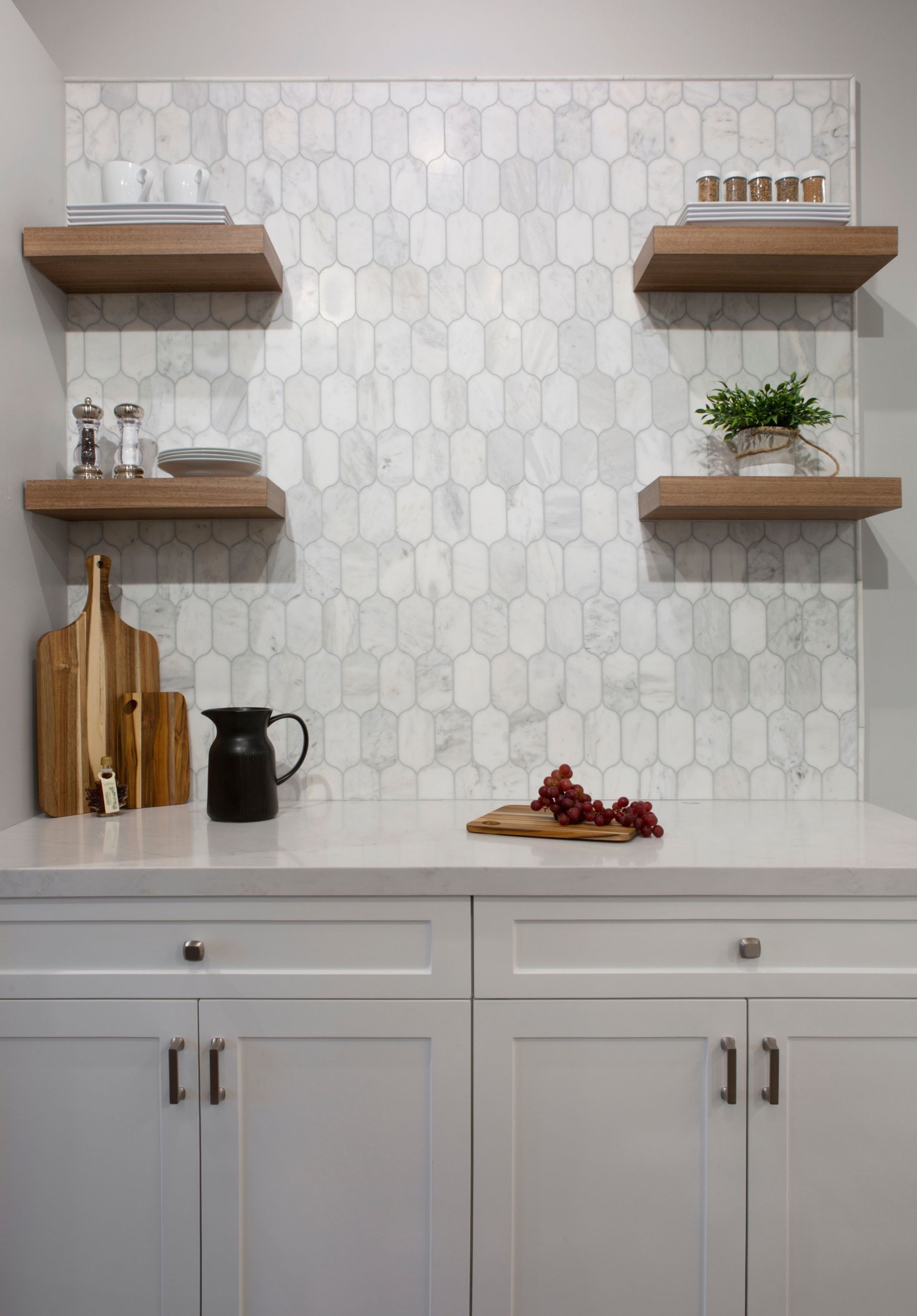 White cabinets with marble backsplash, floating shelves, and countertop with decor.