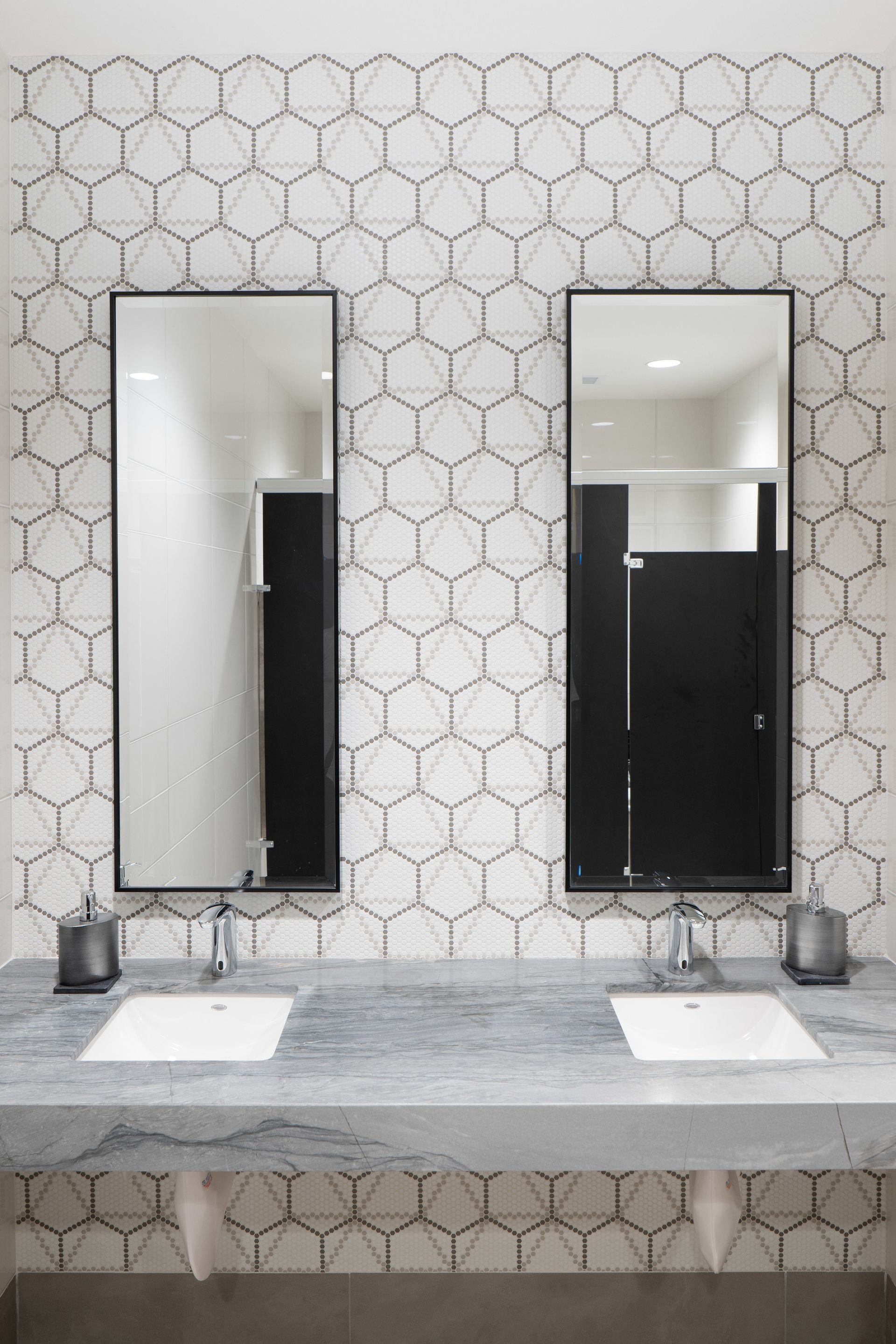Two sinks with mirrors in a bathroom, hexagon tile wall, black framed mirrors.