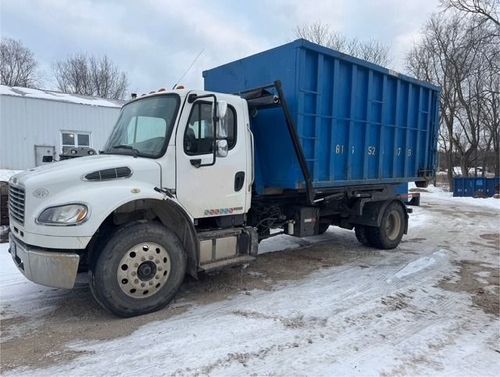 White truck with a blue dumpster on a snowy road.