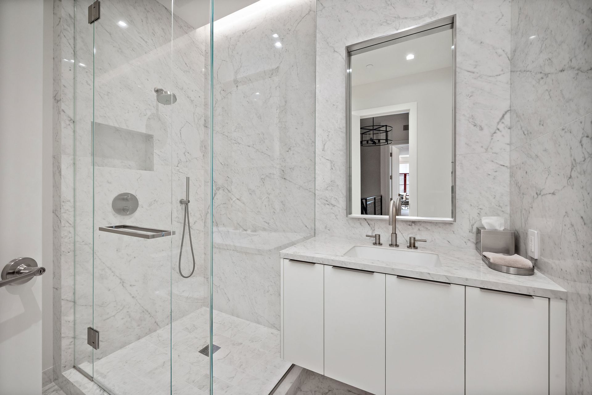 Modern white marble bathroom with glass shower, white vanity, and large mirror.