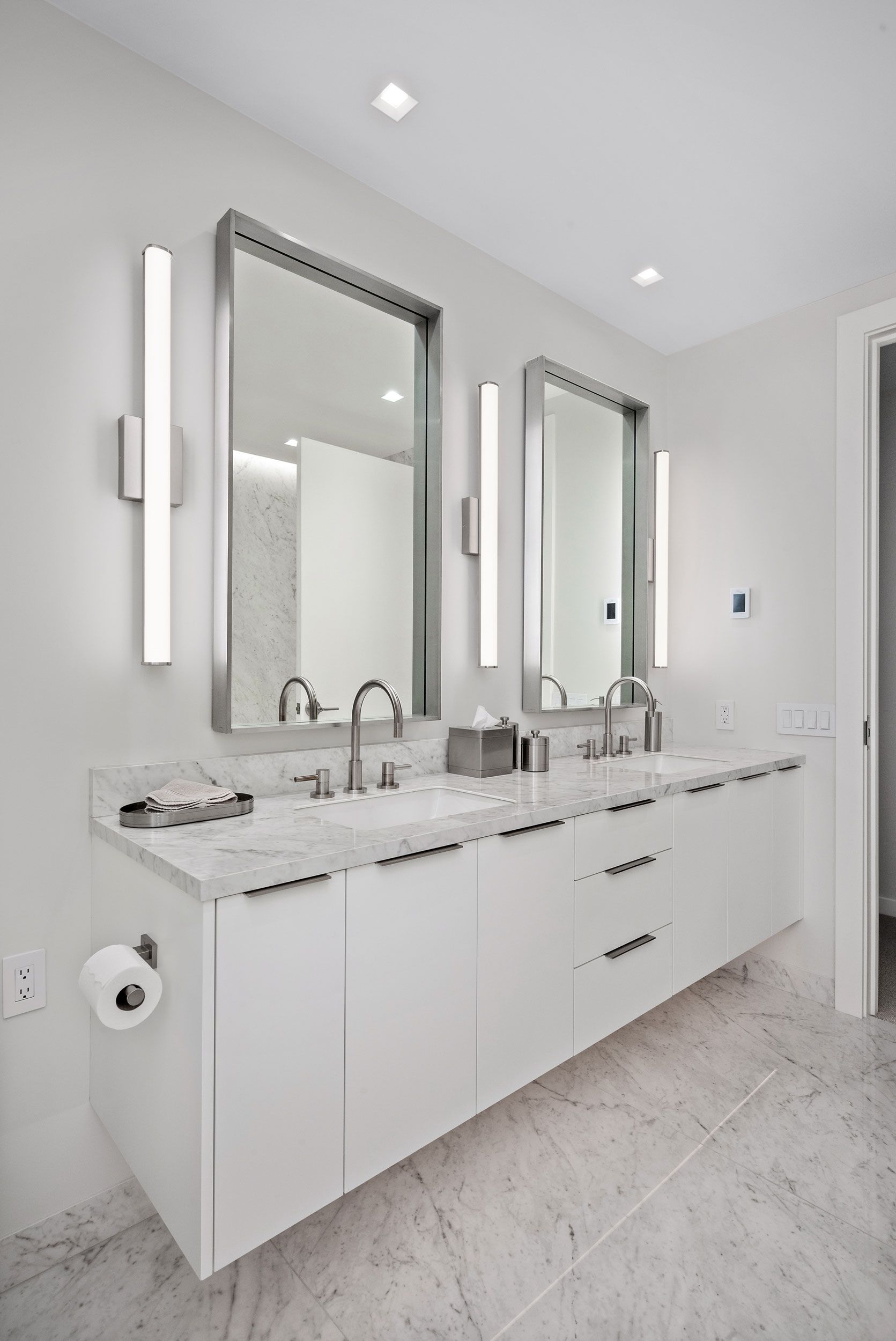 White bathroom with double vanity, mirrors, and sconces.