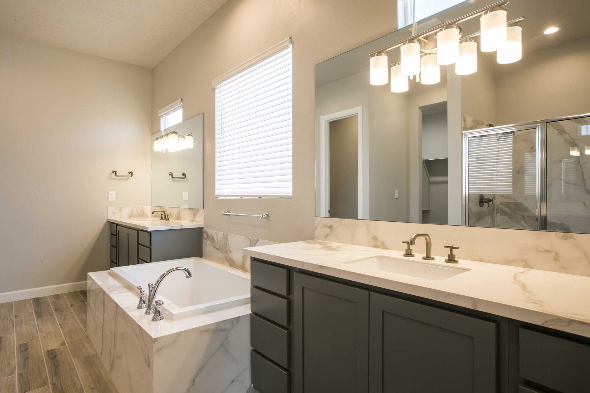 Spacious bathroom with gray cabinets, marble countertops, large mirror, and a bathtub.