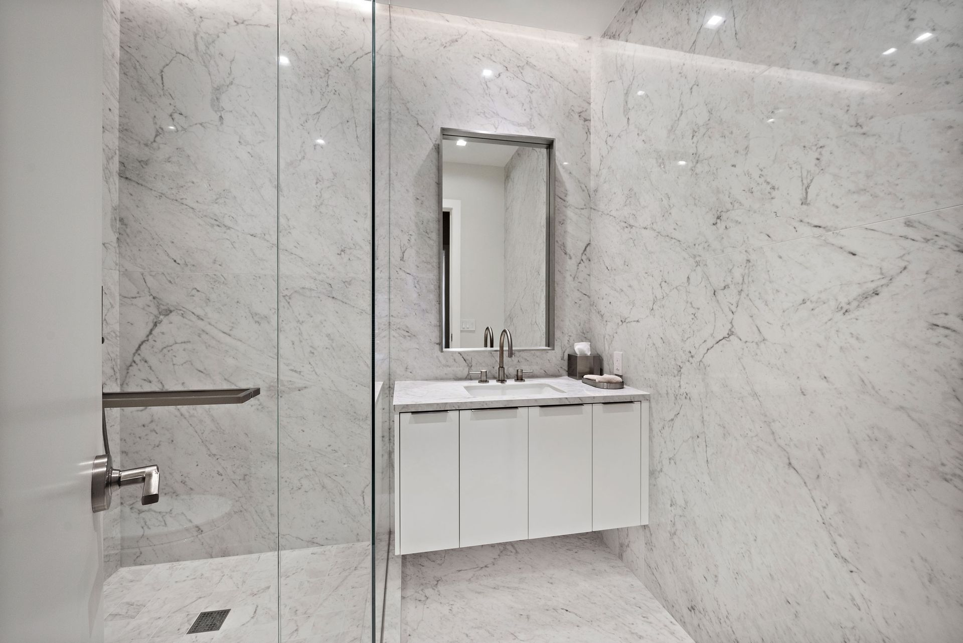 Modern bathroom with marble walls, glass shower, white vanity, and rectangular mirror.