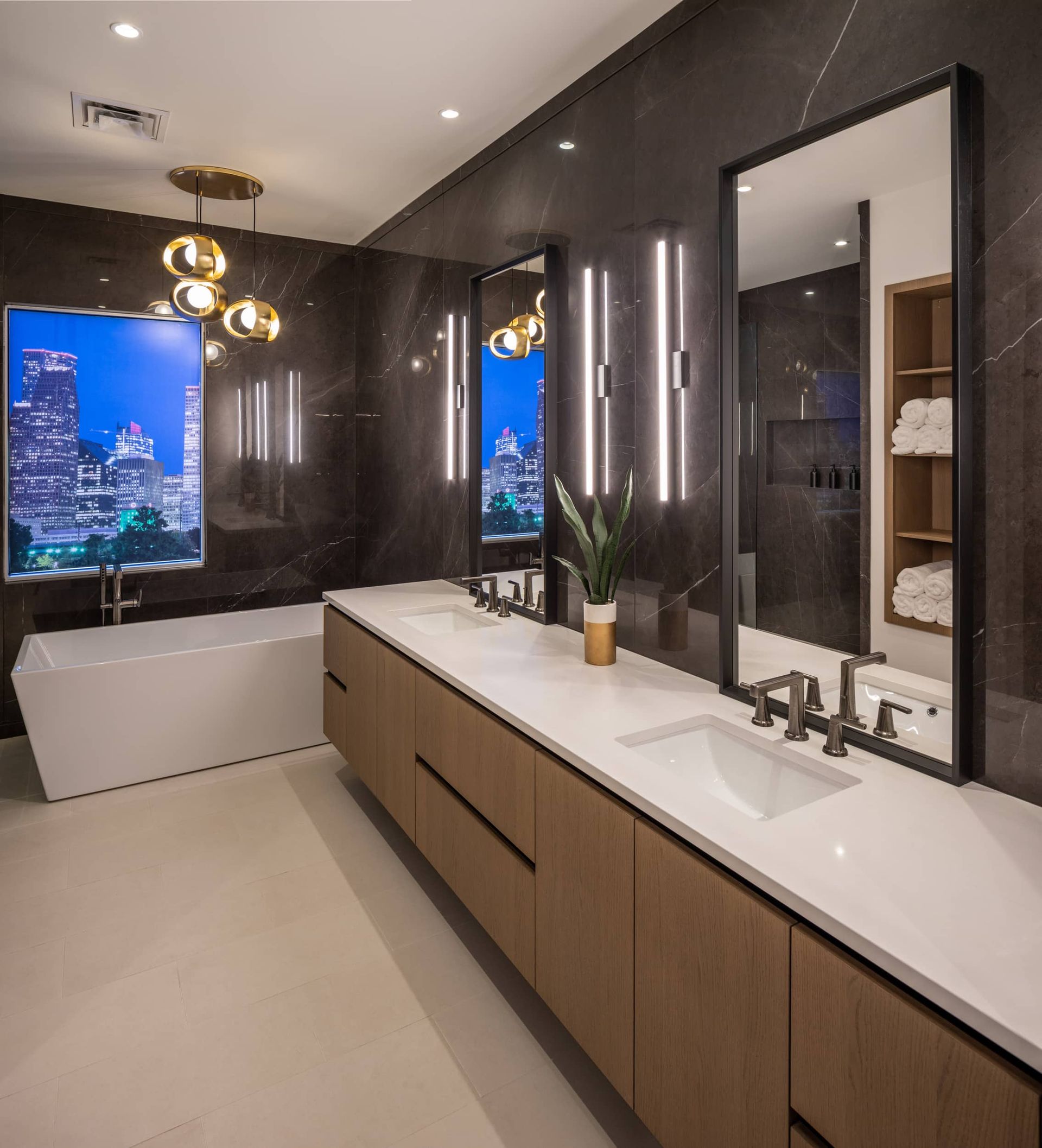 Modern bathroom with a bathtub, double vanity, and cityscape view through a window.