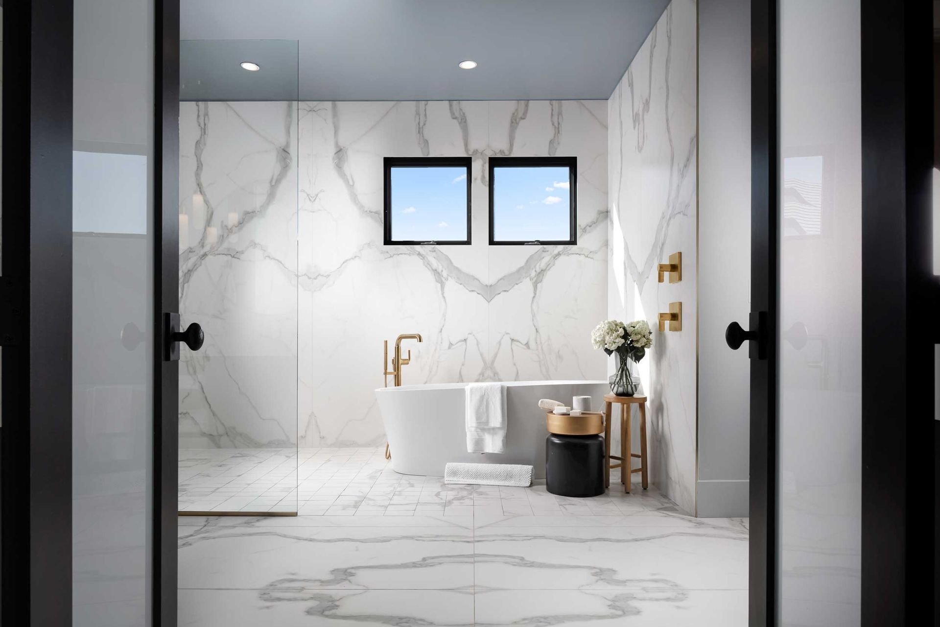 Luxury bathroom with marble walls, a freestanding tub, and small windows.