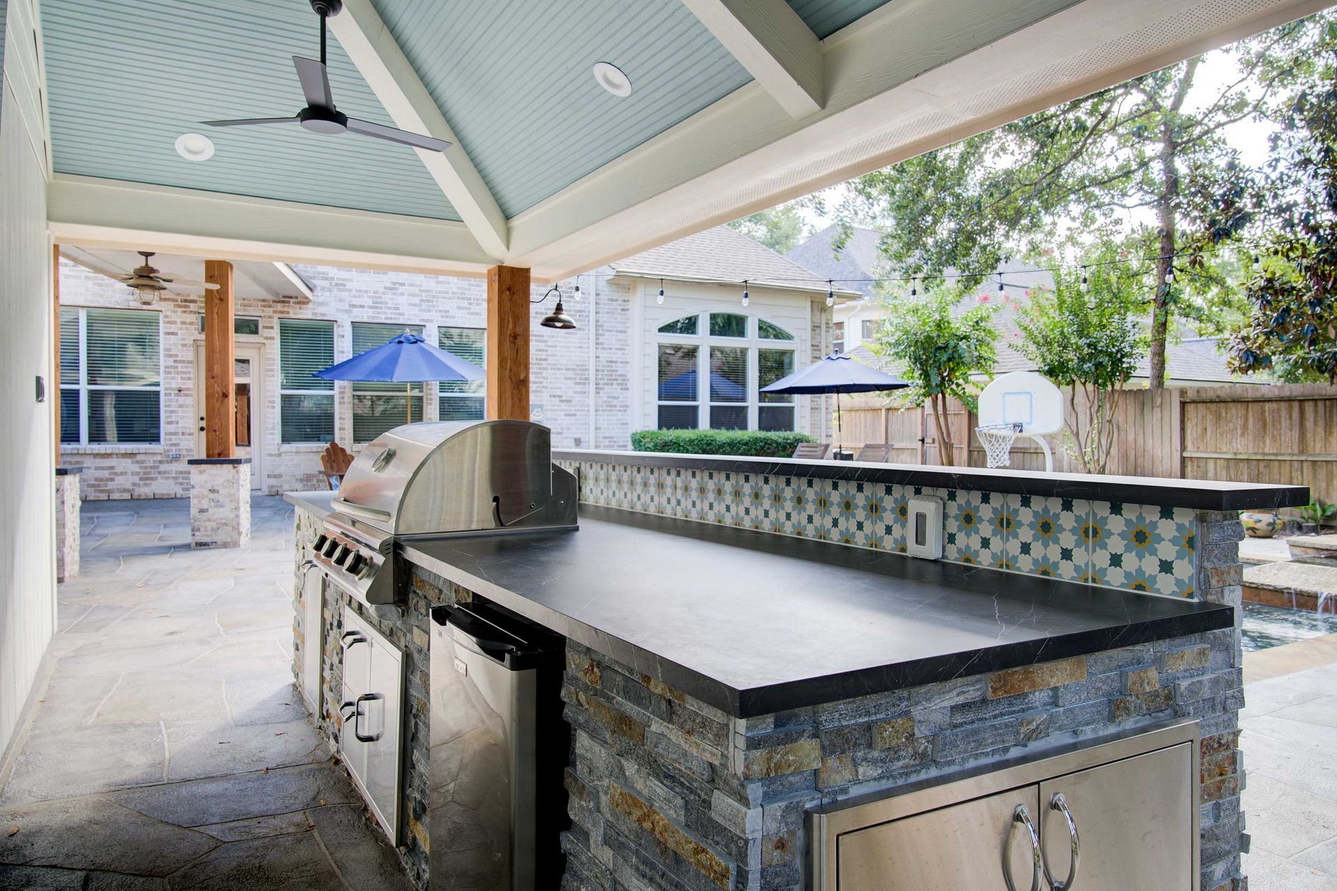Outdoor kitchen with a grill, countertop, and stone facade, under a covered patio with a ceiling fan.