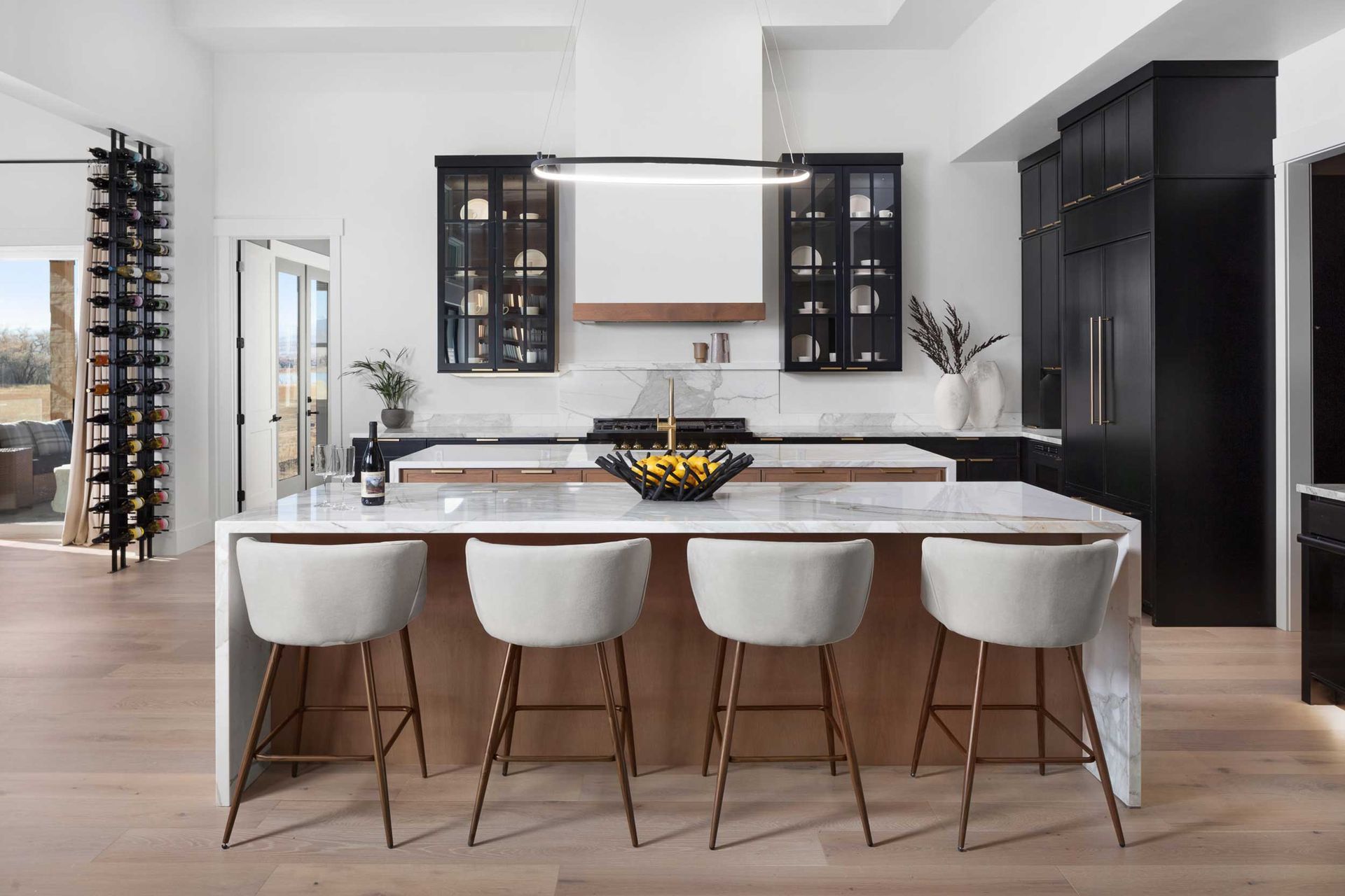 Modern kitchen with island, seating, black cabinetry, wine rack, and light wood floors.
