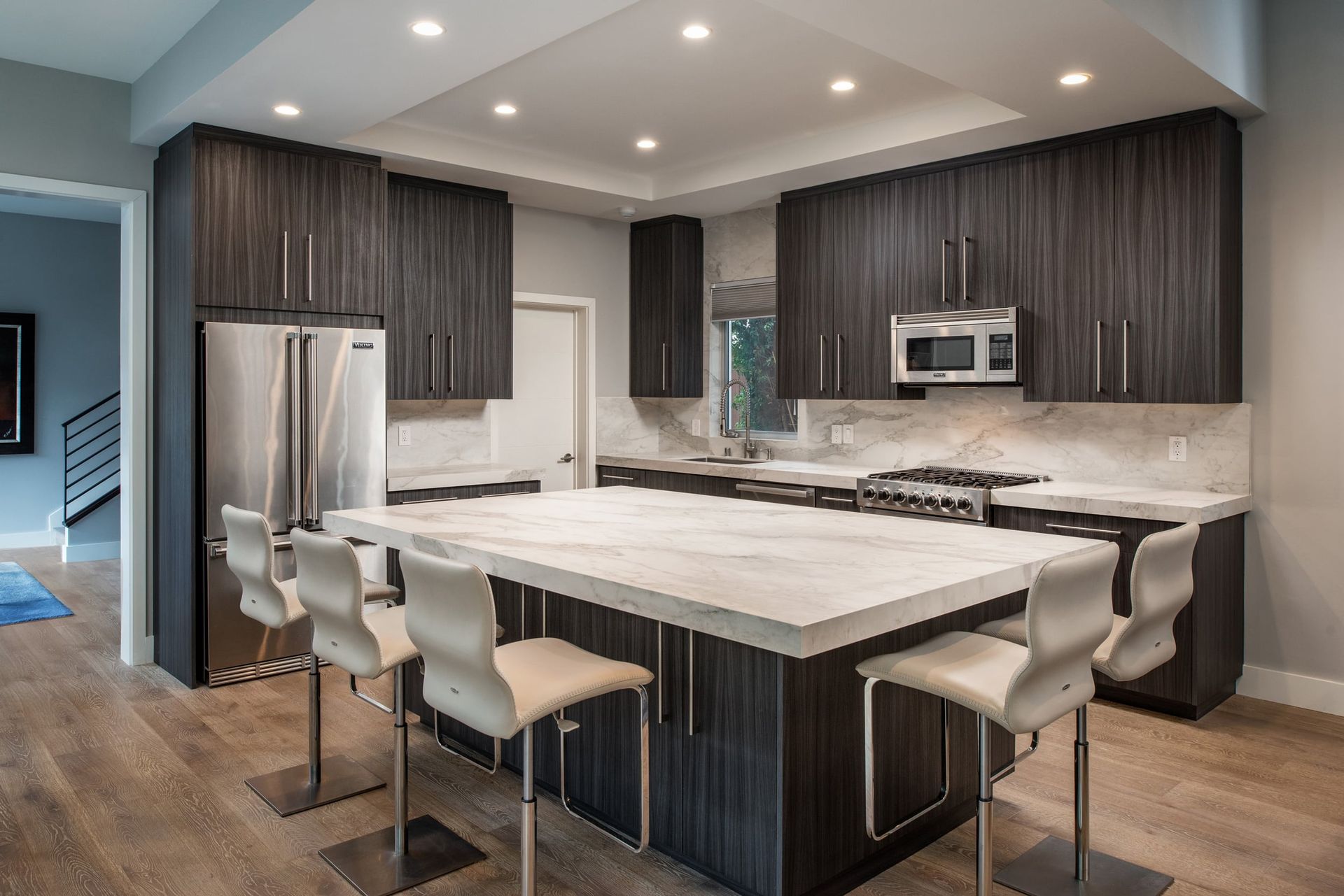 Modern kitchen with dark wood cabinets, stainless steel appliances, and a large white island with seating.