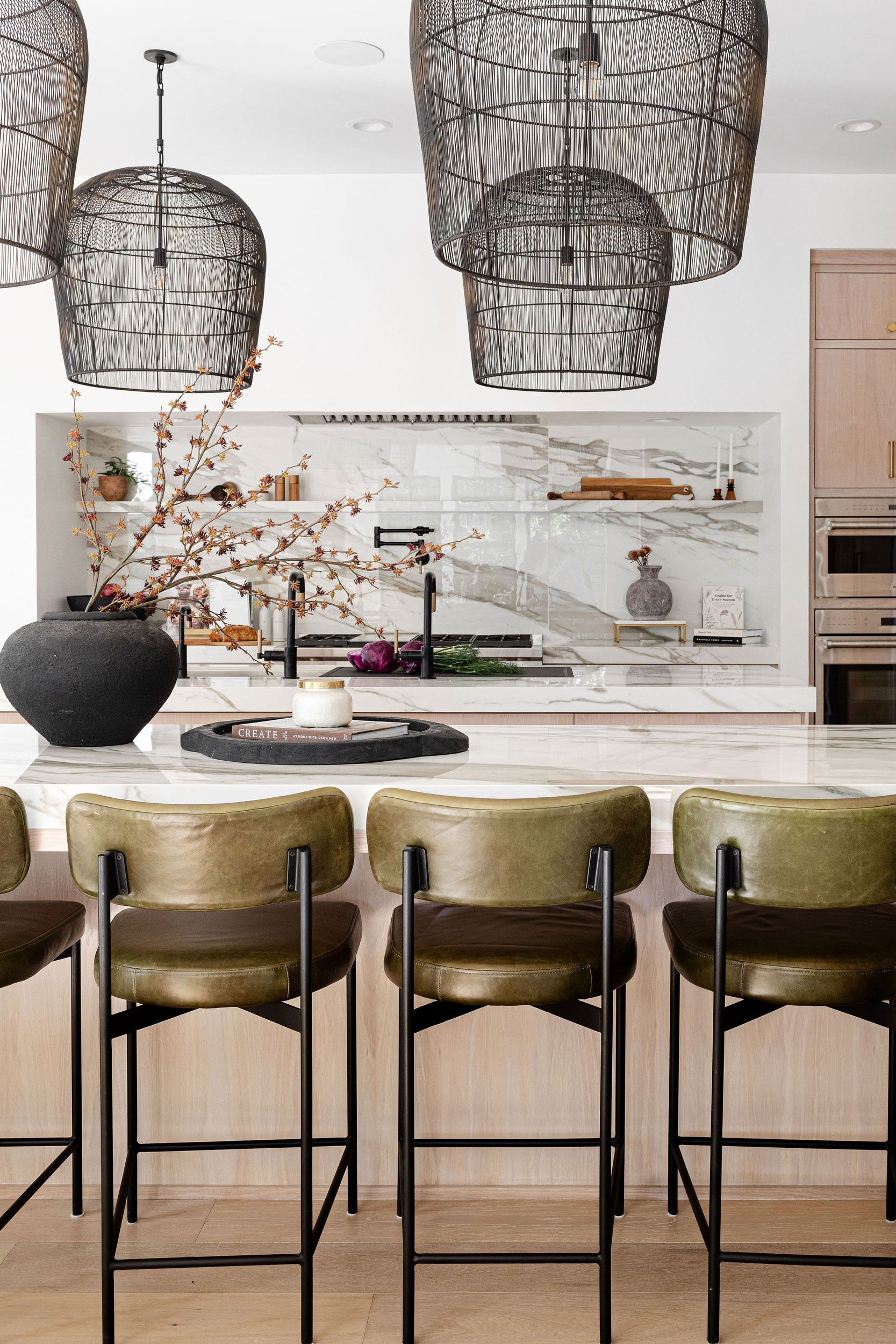 Kitchen with a marble countertop island and brass-colored bar stools. Woven pendant lights hang above.