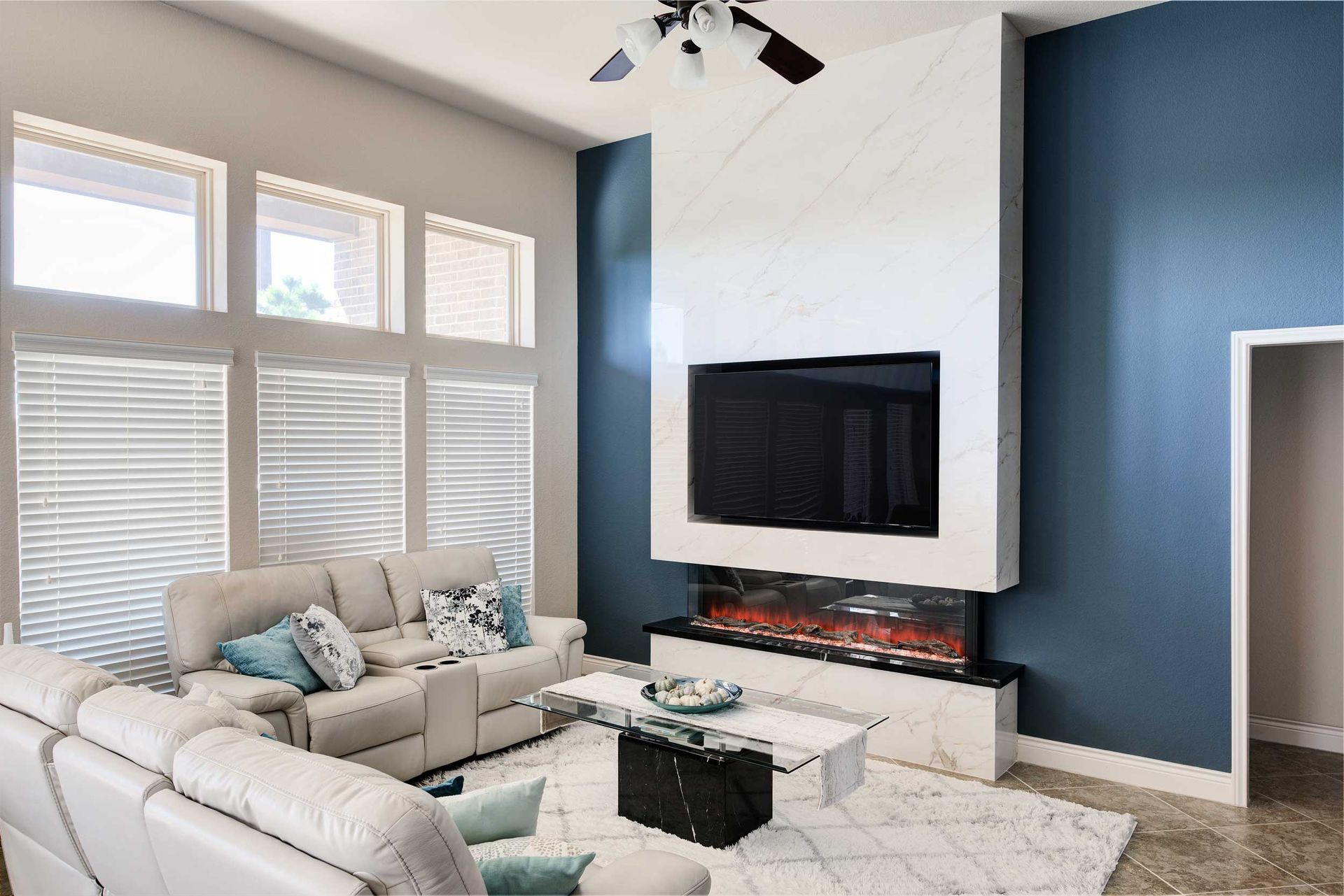 Living room with white sectional sofa, blue accent wall, fireplace, large TV, and rug.