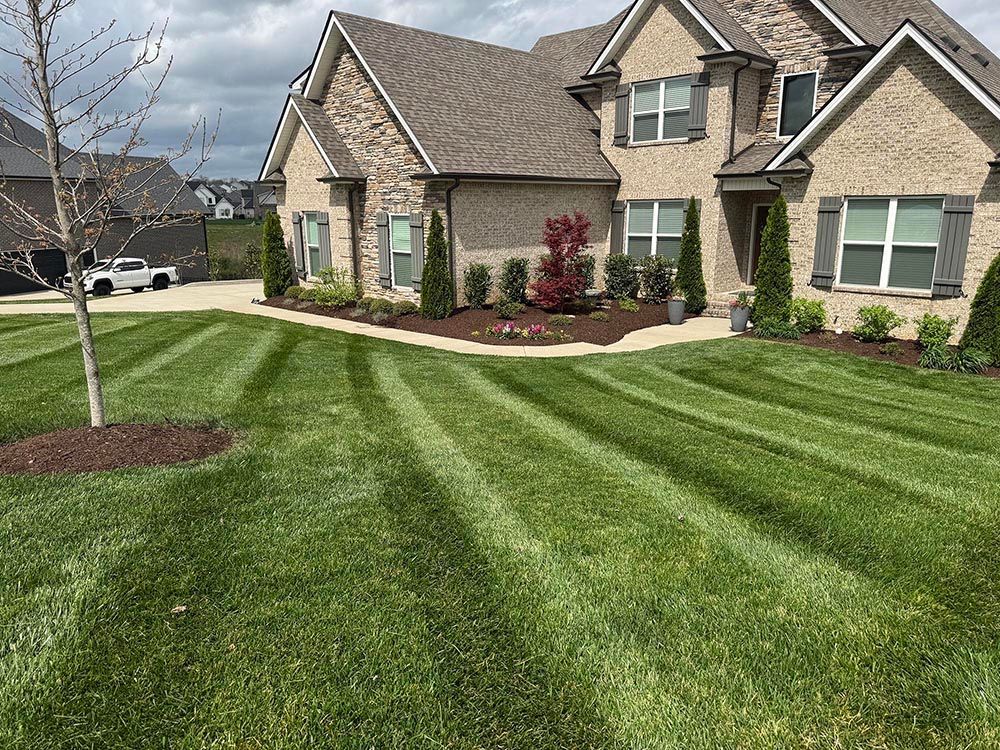 Green lawn with striped mowing pattern in front of a two-story brick house.