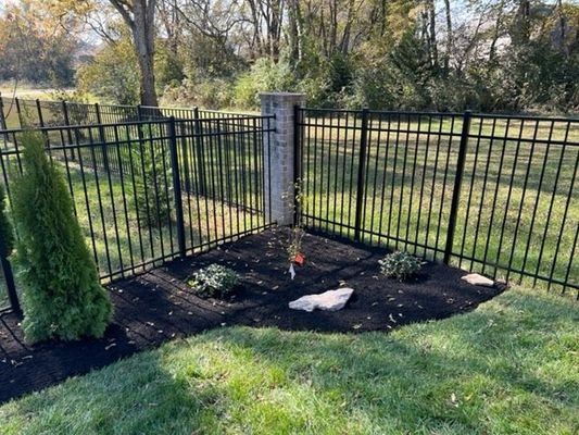 Black metal fence with a corner post, landscaping in front, and green grass.