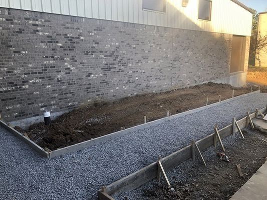 A concrete form borders gravel and soil along a brick building; construction.