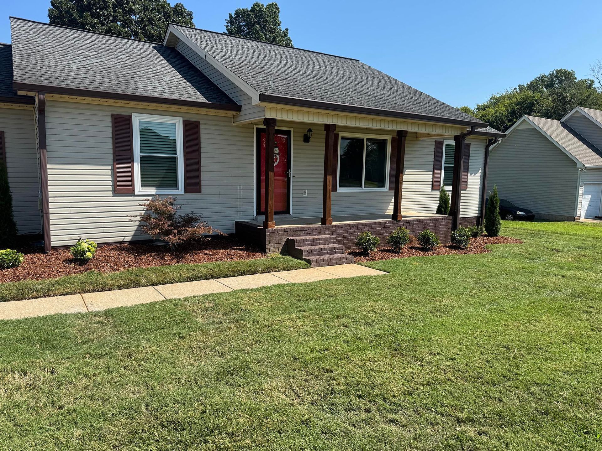 Ranch-style house with tan siding, brown trim, and a red front door; green lawn and blue sky.