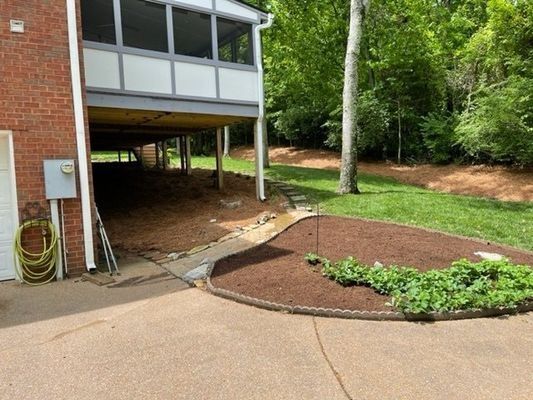 Backyard with deck above, mulched garden bed, and a driveway.