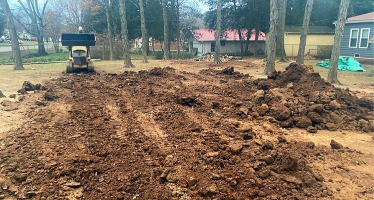 Yellow bulldozer moving dirt in a yard with houses and trees in the background.