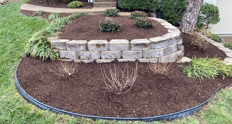 Curved brick retaining wall with mulch and plants, set in a green lawn.
