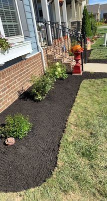 Dark mulch in a flower bed bordering a house with a brick facade and green lawn.
