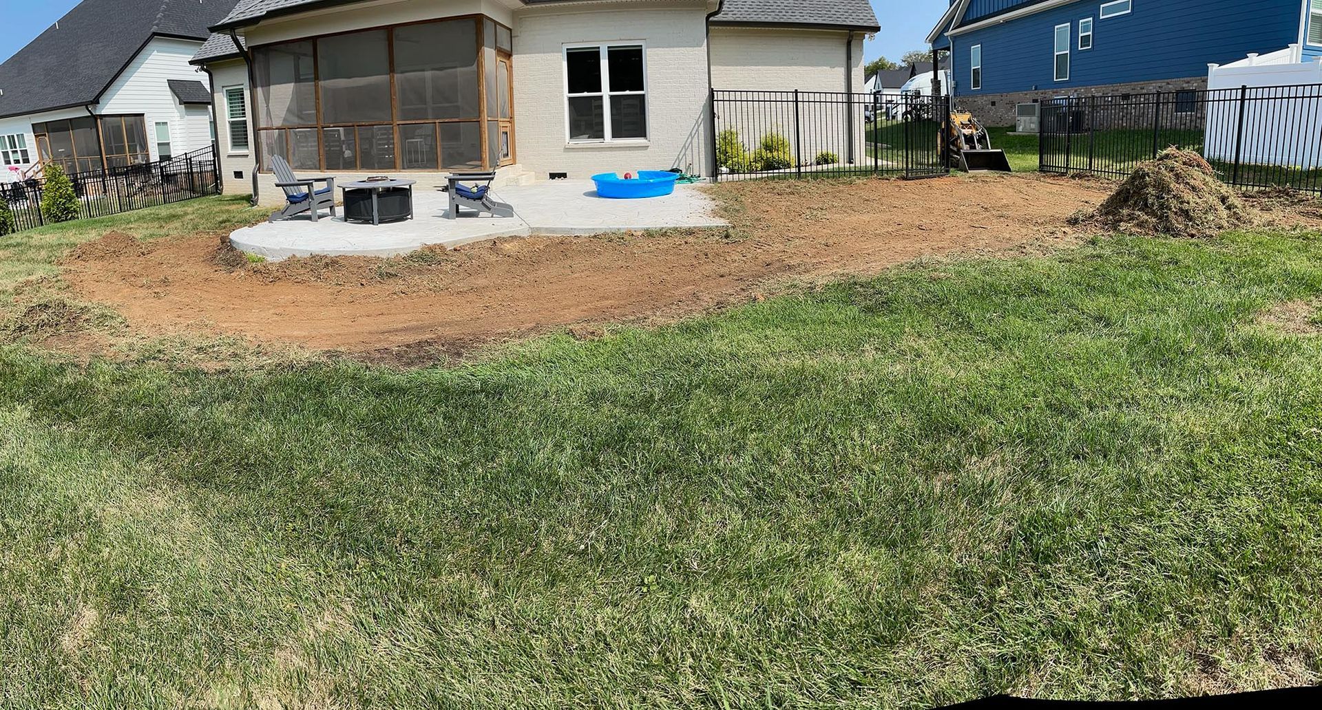 Backyard with a concrete patio, bare dirt, and grass.