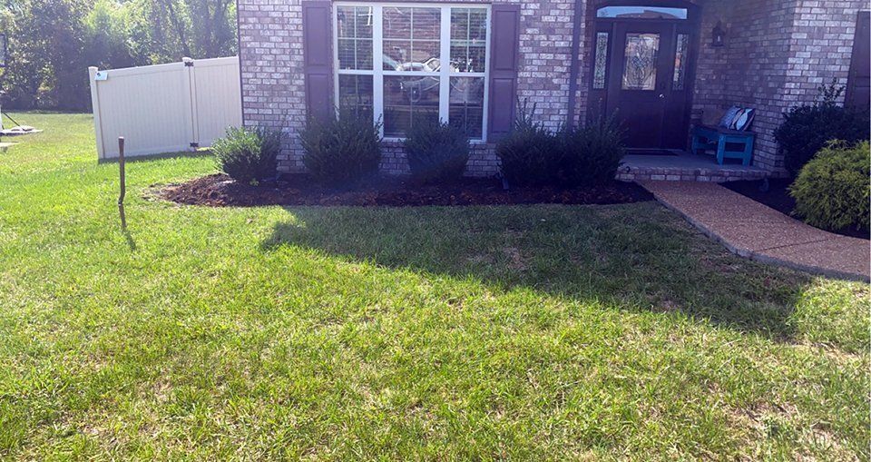 Front yard of a brick house with green lawn, landscaping, and a pathway leading to the front door.