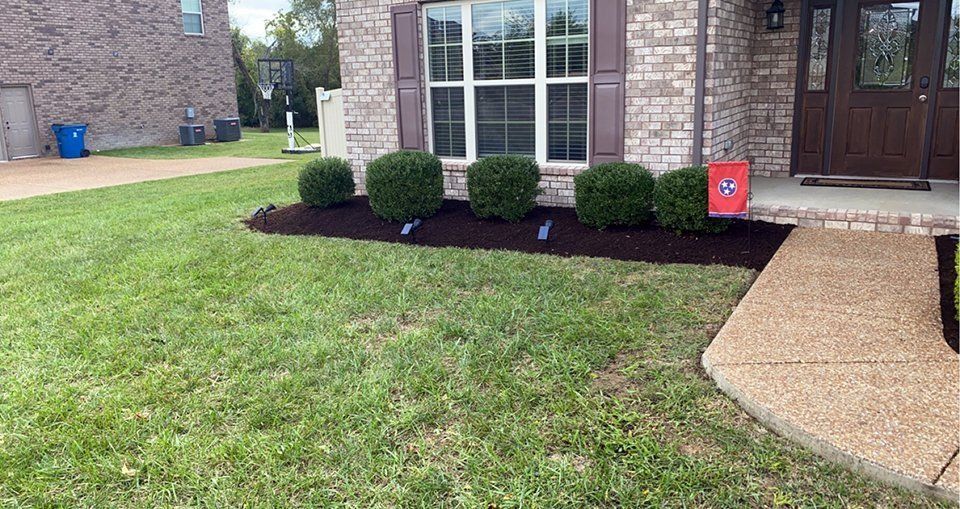 A well-manicured lawn with a flower bed of bushes in front of a brick house.