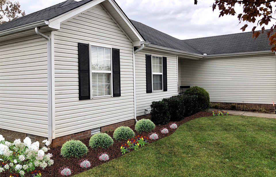 Curb appeal: White-sided house with black shutters, dark roof, and a landscaped garden with green bushes and lawn.