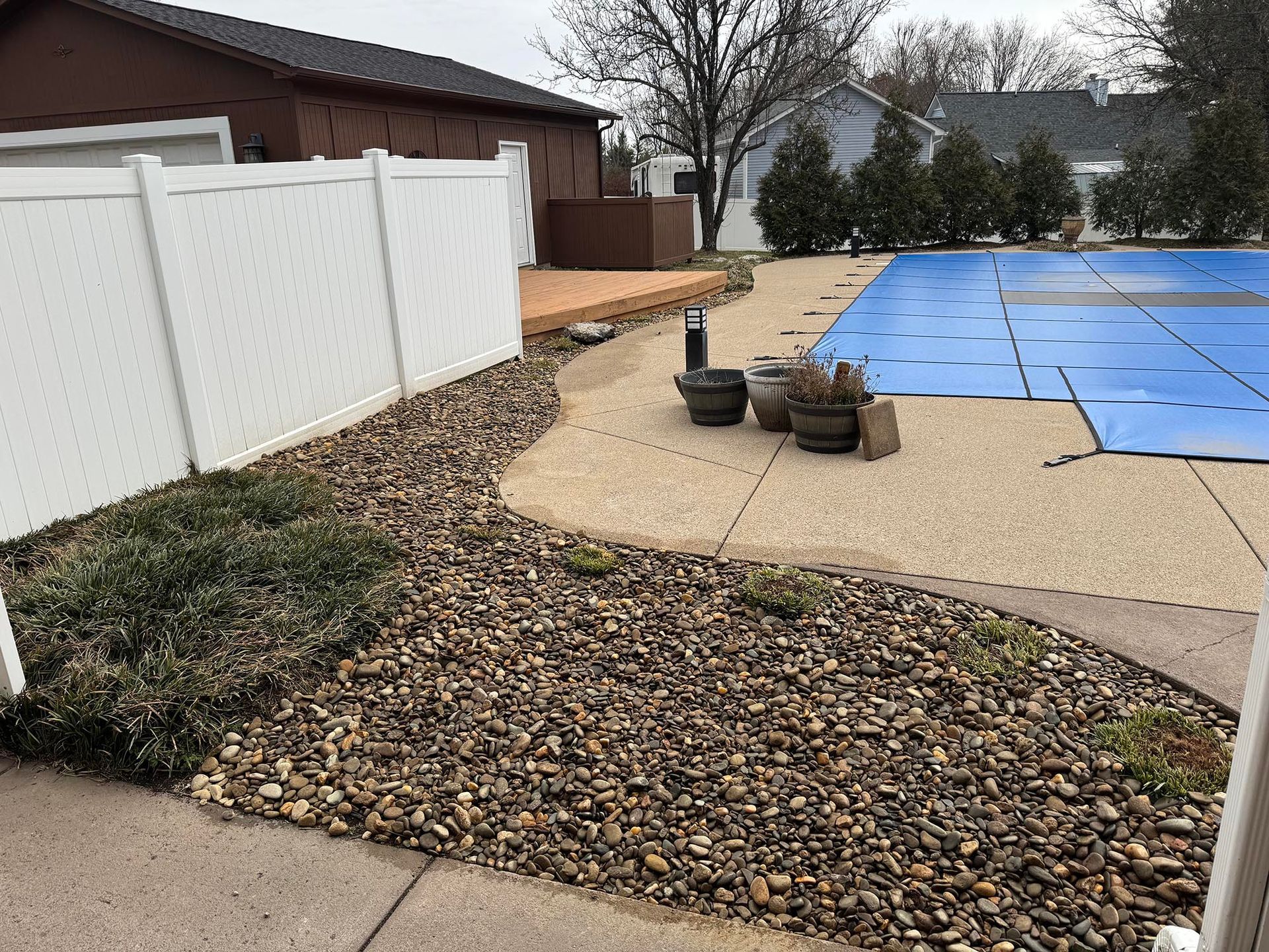 Stone landscaping bed and patio border pool. White fence borders left.