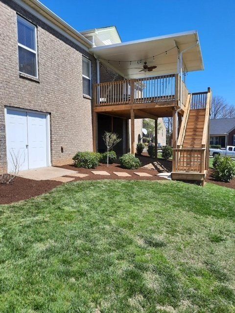 Backyard with a two-story deck, stairs, green grass, and brick house.