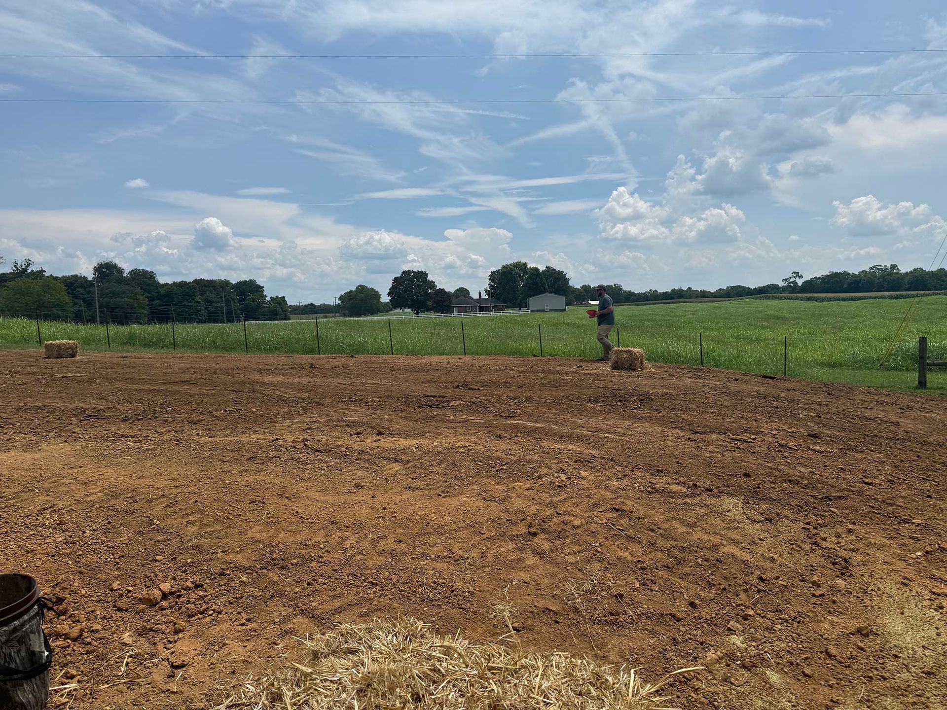 Person in a field; preparing soil for planting crops; rural outdoor setting under a cloudy sky.