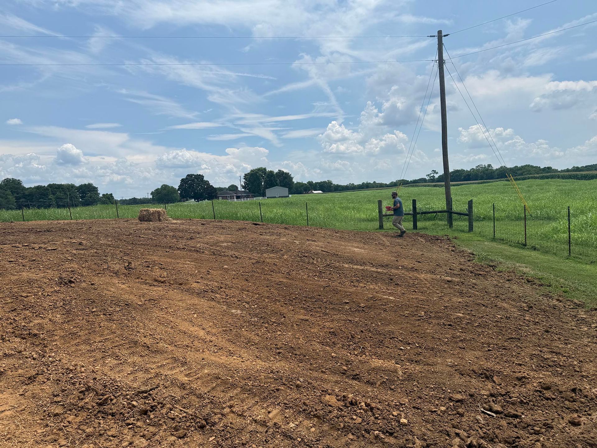 Plowed field with a person walking by a fence, under a blue sky.
